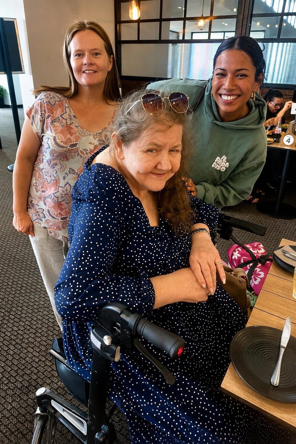 Three women smiling together around a table at a cafe