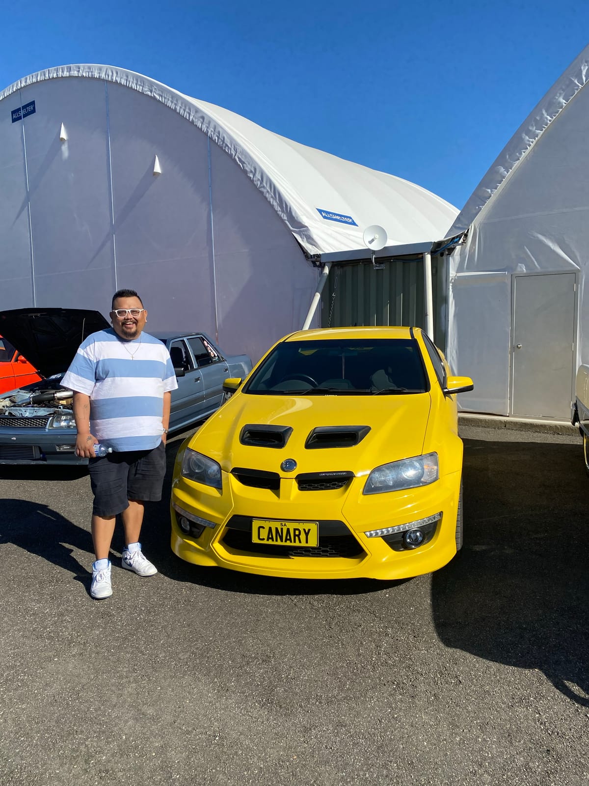 A participant standing beside a bright yellow car at a car show