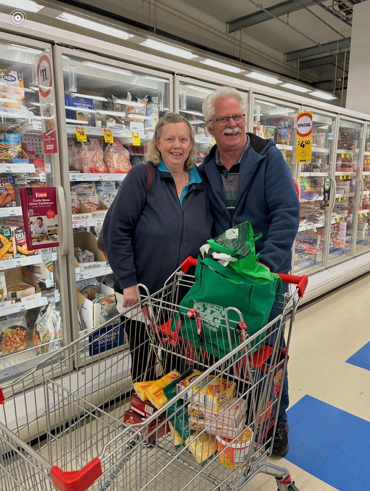 Two people smiling beside a full trolley during a grocery shop