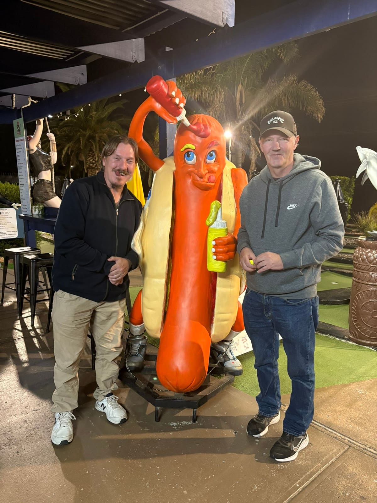Two team members posing together with a giant novelty hot dog statue on an outing