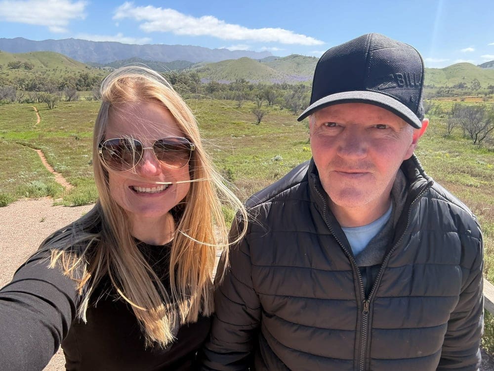 A support worker and participant smiling together on a walk in the hills